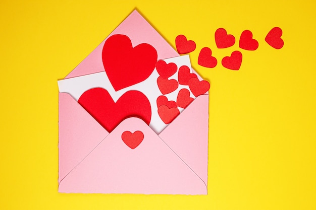 Valentine's Day card. Paper red hearts fly out of pink paper envelope on yellow background . Paper art on valentine day. paper cut and craft style. Space for text. concept of Valentine's Day