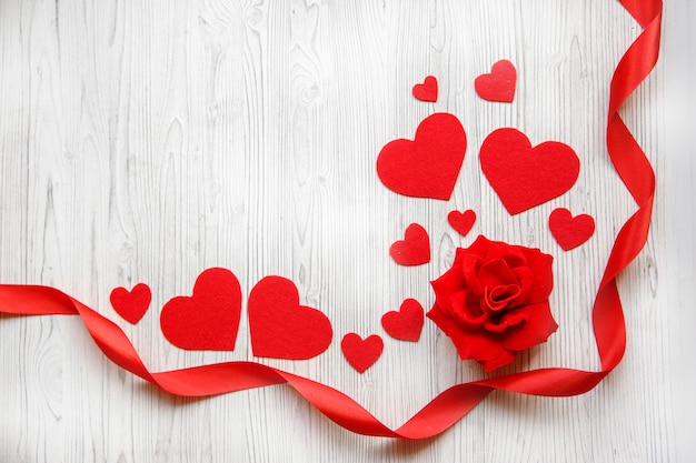 Valentine's day card, red hearts, ribbon and red rose on a white wooden background. Space for text