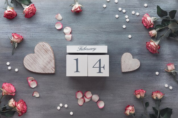 Valentine's day celebration, flat lay with wooden calendar, pink roses and wooden hearts on dark