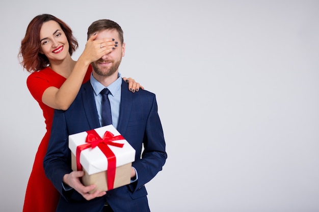 Valentine's day, christmas or surprise concept - woman surprising her boyfriend with gift and copy space over white background