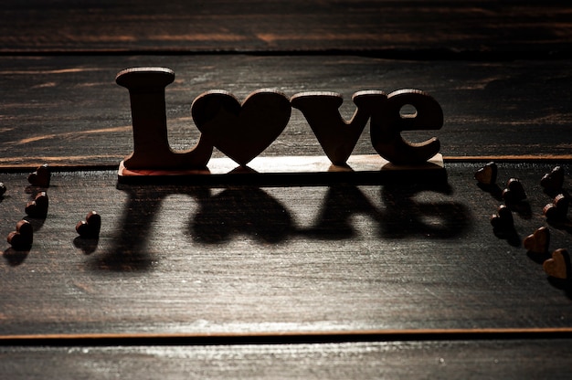 Photo valentine's day composition with hearts and silhouette of the word love on wooden board