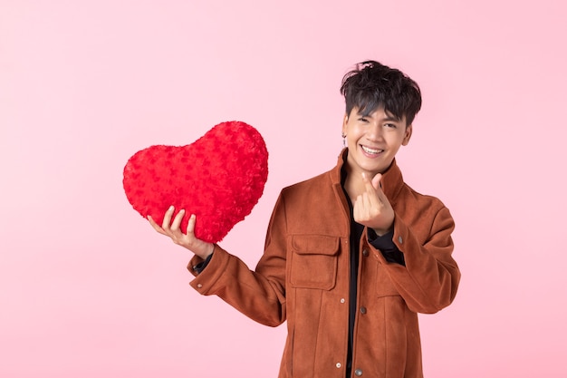 Valentine's day concept, Asian a man handsome young holding a red heart shaped pillow in love isolated on pink blank copy space studio background.