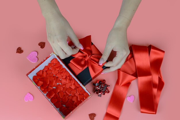 バレンタインデーのコンセプト手作りの赤いリボンでギフトを梱包する女性の手のクローズアップ