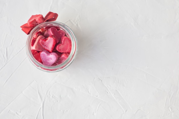 Foto concetto di san valentino. vaso con piccoli cuori rossi e rosa su uno sfondo chiaro.
