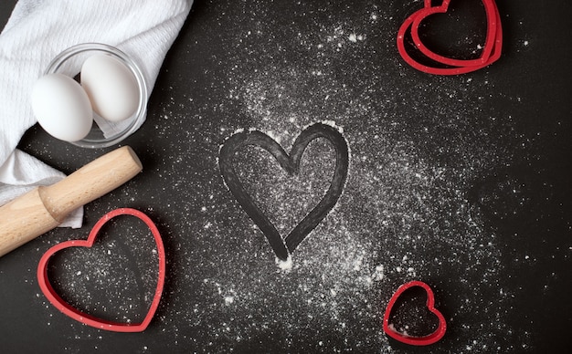 Valentine's day cooking composition with the finger-drawn heart
on the scattered flour on the dark background. flat lay, top
view.