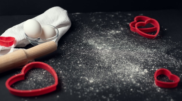 Valentine's Day cooking composition with scattered flour on the dark background.