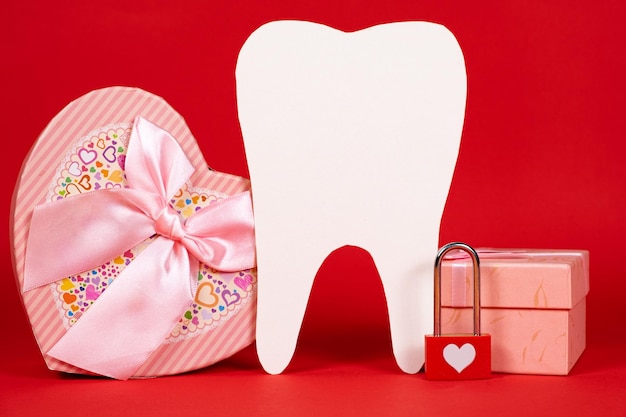 День святого Валентина в стоматологии большой белый зуб сердце и коробки с подарками на красном фоне