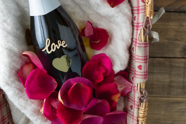 Valentine's Day. Gift basket with champagne bottle with LOVE inscription. Decoration with red rose petals. Copy space.