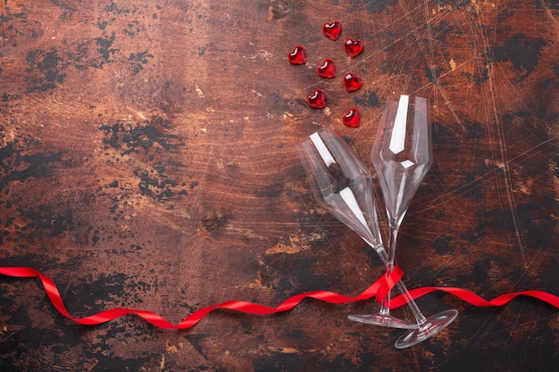 Открытка на день Святого Валентина с бокалами для шампанского, декоративными сердечками и красной лентой на деревянном фоне Копирование пространства Вид сверху