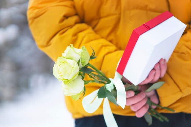 バレンタインデーの休日。彼の背中の後ろに、贈り物とバラ、花のギフトボックスのクローズアップ花束を持っている若い男の男。