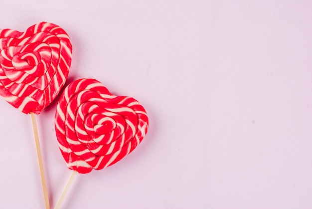 Valentine's day light pink background greeting card concept Two red heart lollipops or sweet candy on sticks 