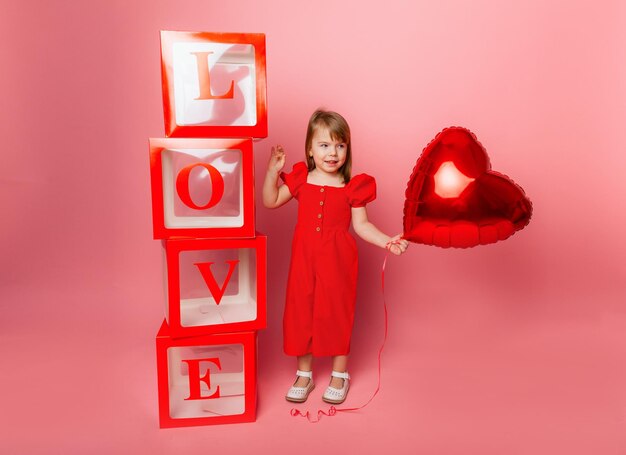 Valentine's day, Little girl in holding a big balloon in the shape of a heart on a pink background.