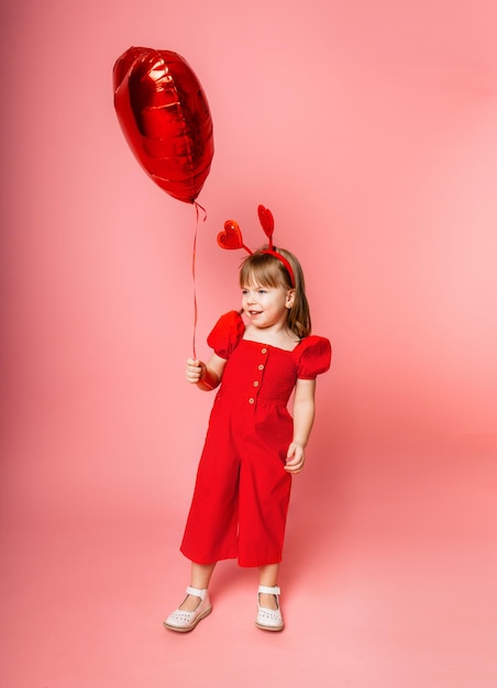 Valentine's day, Little girl in holding a big balloon in the shape of a heart on a pink background.