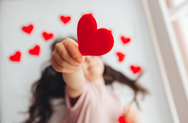 Valentine's Day a little girl lying at home on a white bed among hearts smiling and laughing with happiness congratulating on the holiday