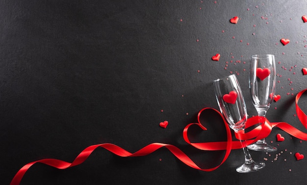Concetto di san valentino e amore fatto da bicchieri di champagne e cuori rossi su fondo di legno nero