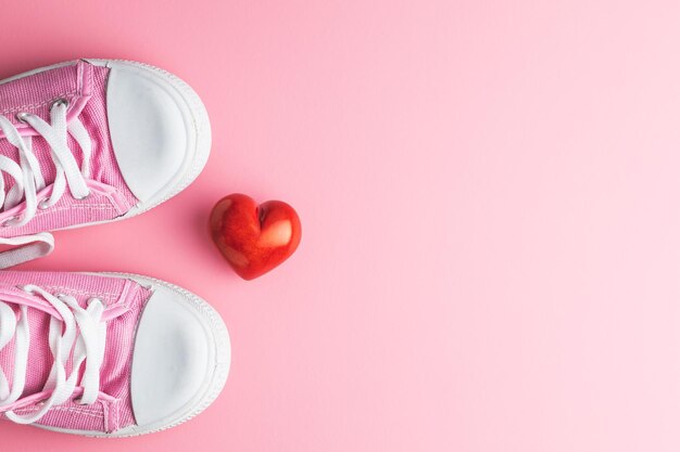 Valentine's day love concept pink sneakers and red heart on pink background top view