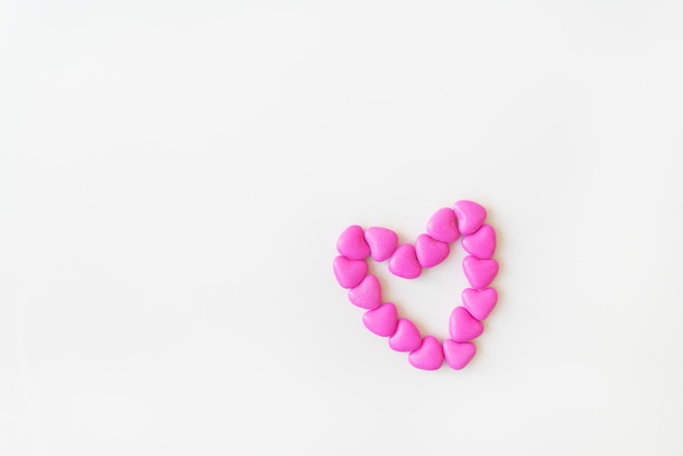 Valentine's day pattern background flat lay top view of heart shaped pink candies scattered on white background. Place for an inscription.