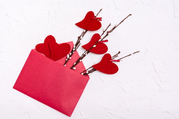 День Святого Валентина. Красные сердца из войлока на ветвях ивы и рядом в открытом красном конверте. Копировать пространство