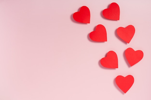 Valentine's day. Red paper hearts with shadow on pink surface. Flat lay, top view, copy space