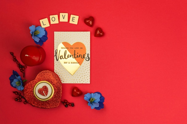 赤い背景、花、キャンドル、単語の愛、グリーティングカード、上面図、コピースペースの写真に赤いハートとバレンタインデーのロマンチックなコンセプト