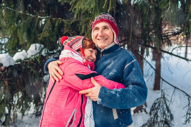 Valentine's Day. Senior family couple hugging in winter forest. Happy man and woman walking outdoors.