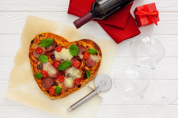 Regolazione della tavola di san valentino. pizza cuore con vino, bicchieri e confezione regalo