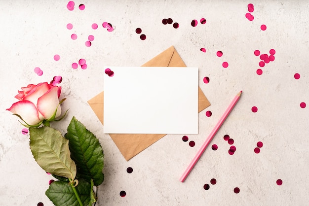 Photo valentine's day. top view of blank letter and envelope with pink pencil, confetti and rose