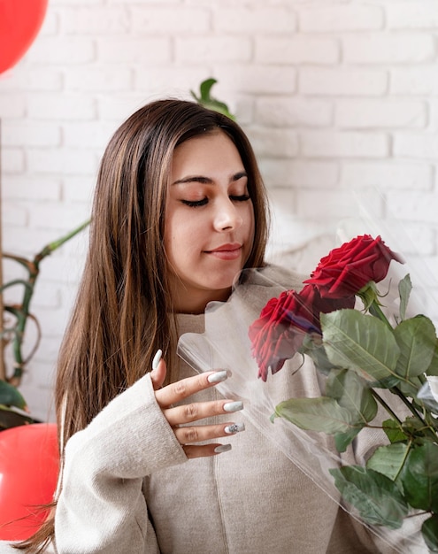 San valentino, festa della donna. giovane donna castana caucasica seduta nel letto che celebra il giorno di san valentino profumato di rose rosse