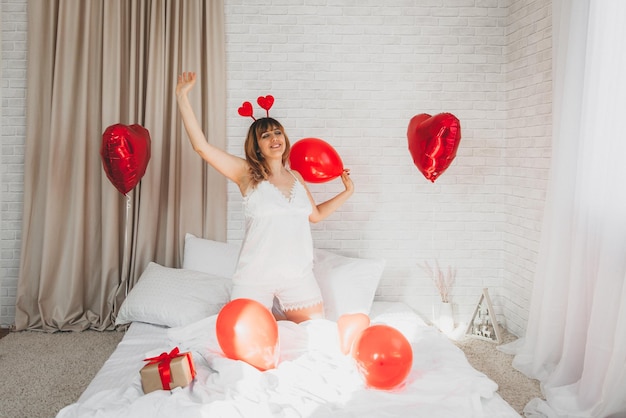 Valentine's day, women's day. young caucasian girl sitting in bed and celebrating valentine's day holding a heart-shaped balloon in her hands