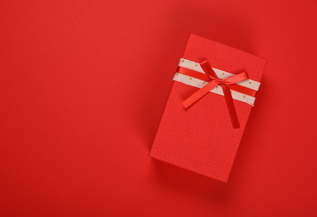 사진 빨간색 포장지 배경 위에 리본 쉬폰 활과 닫힌 생생한 빨간색 선물 상자의 발렌타인 템플릿, 바로 위의 평평한 평신도, 높은 평면도를 닫습니다.
