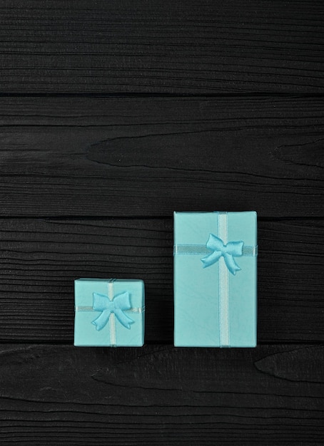 Valentine template of two closed small blue gift boxes with ribbon bows over black wooden table background, close up flat lay, elevated top view, directly above