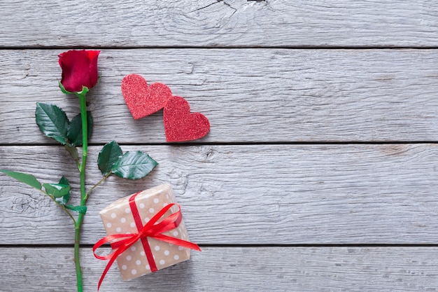 Valentine with red rose flower, handmade paper hearts and present box on rustic wood