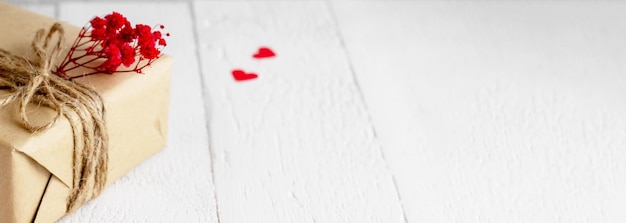Баннер ко Дню святого Валентина 39 Подарочная коробка из крафт-бумаги с сердечками и красными цветами на белом деревянном фоне