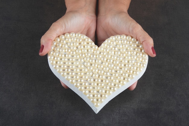 Sfondo di san valentino con mano che tiene il cuore con perle bianche.