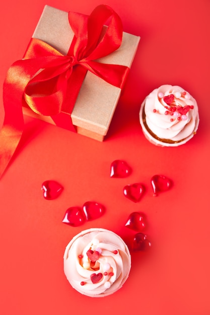 Valentines cupcakes cream cheese frosting decorated with heart candy and gift box on the red background. Valentine s day concept. Top view.