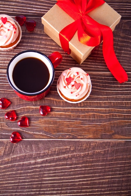 Valentines cupcakes cream cheese frosting decorated with heart candy, mug of coffee and gift box. Valentine s day concept. Copy space. Top view.