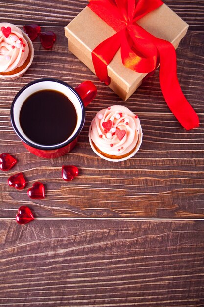 Valentines cupcakes roomkaas glazuur versierd met hart snoep, mok koffie en geschenkdoos. Valentijnsdag concept. Kopieer ruimte. Bovenaanzicht.