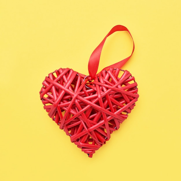 Фото День святого валентина фон. красное плетеное сердце на желтом фоне. копирование пространства, вид сверху. валентинки