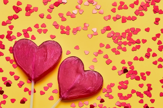 Valentines Day background. Two candy hearts with glitter on yellow backdrop. Top view, copy space