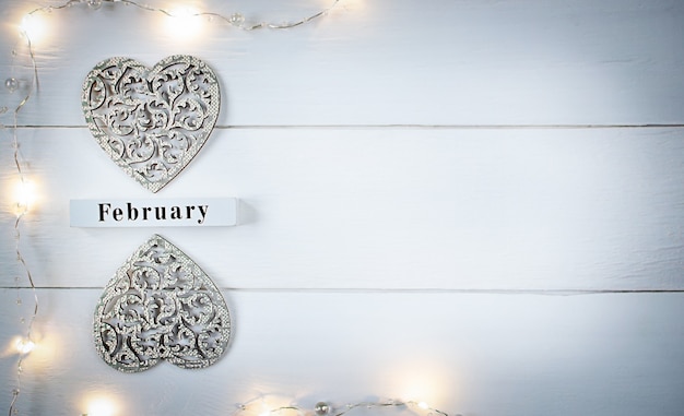 День Святого Валентина фон с резными деревянными сердцами, желтой гирляндой и деревянным календарем на февраль с копией пространства