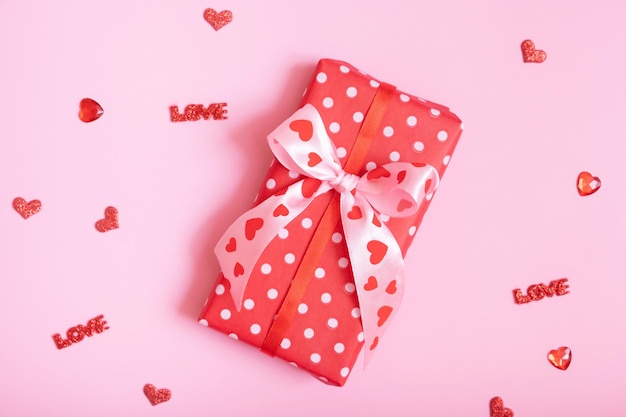 Valentines Day background with gaoft box and red hearts and love words on pink background flat lay