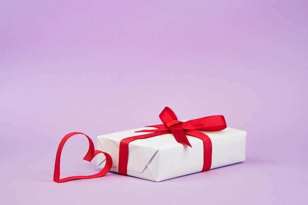 Valentines Day or birthday concept with copy space Red ribbon heart and gift box on purple papper