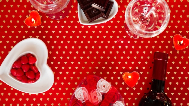 Valentines day. Bottle of vine, glasses, red roses, candles - red background. Love dinner concept