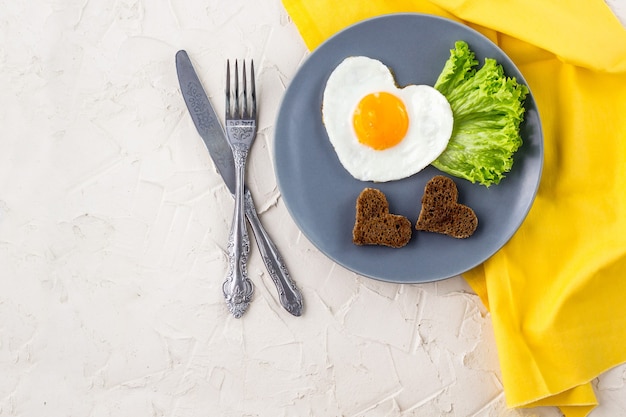 심장 모양의 달걀 프라이와 발렌타인 데이 아침 식사는 회색 접시와 노란색 냅킨에 제공됩니다.