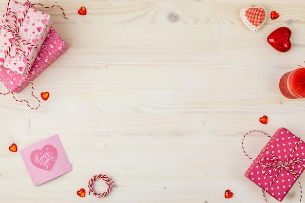 Composizione in san valentino con scatole regalo, cuori diversi e candela su uno sfondo in legno chiaro.