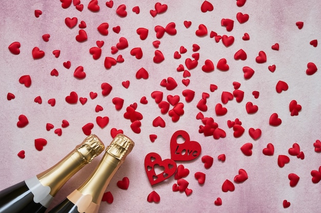 Valentines Day concept. Champagne bottles with red hearts on pink background.