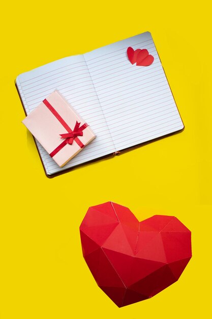 A valentines day concept on a flat lay with a gift box up to the notebook and a heart made of paper