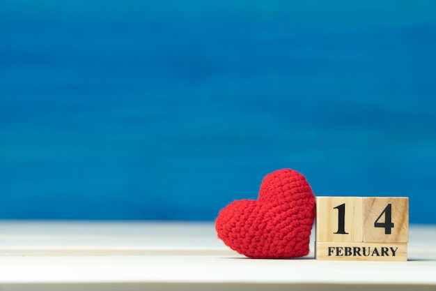 Foto concetto di giorno di san valentino. la mano fa il cuore rosso del filato accanto al calendario del blocco di legno fissato su san valentino data il 14 febbraio