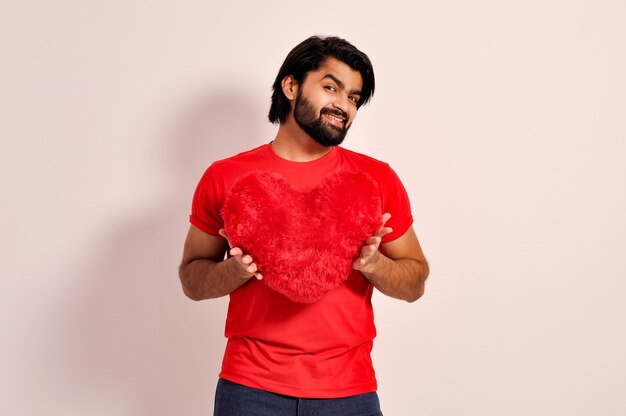 写真 バレンタインデーのコンセプト恋に赤いハート型の枕を保持しているハンサムな若いインド人