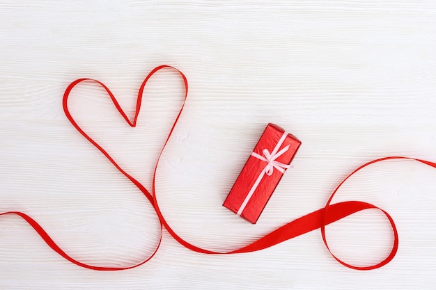 Valentines Day concept. Red heart from ribbon and surprise box on white wooden